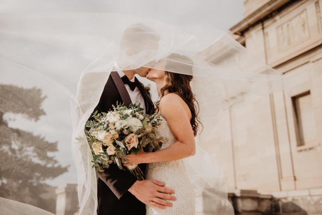 jeunes mariés qui s'embrassent sous un voile de mariage blanc